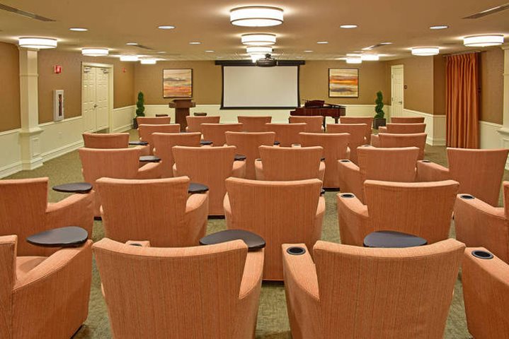 A conference room with peach-colored chairs facing a projector screen and podium at the front