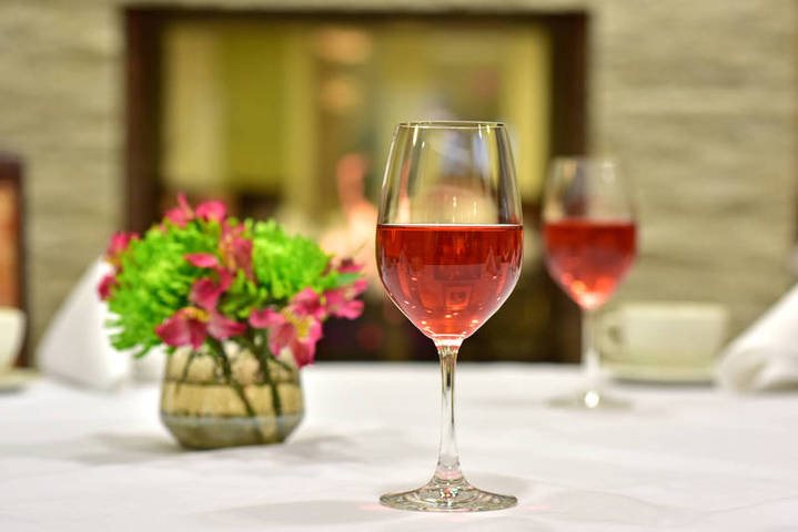Clear wine glass with pinkish rosé wine on a table beside vibrant flowers in a restaurant.