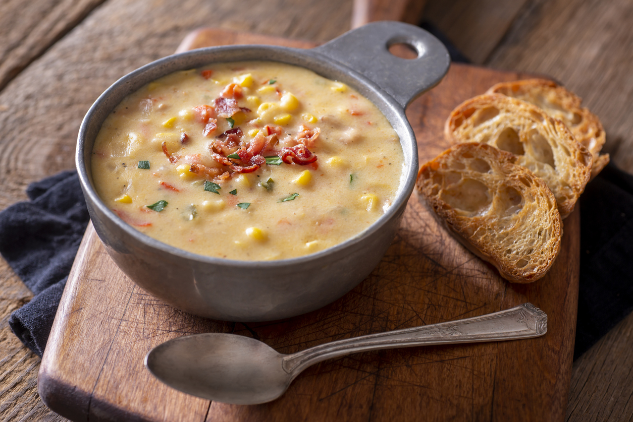 a rustic bowl of creamy corn chowder with bacon and herbs, served with toasted bread slices