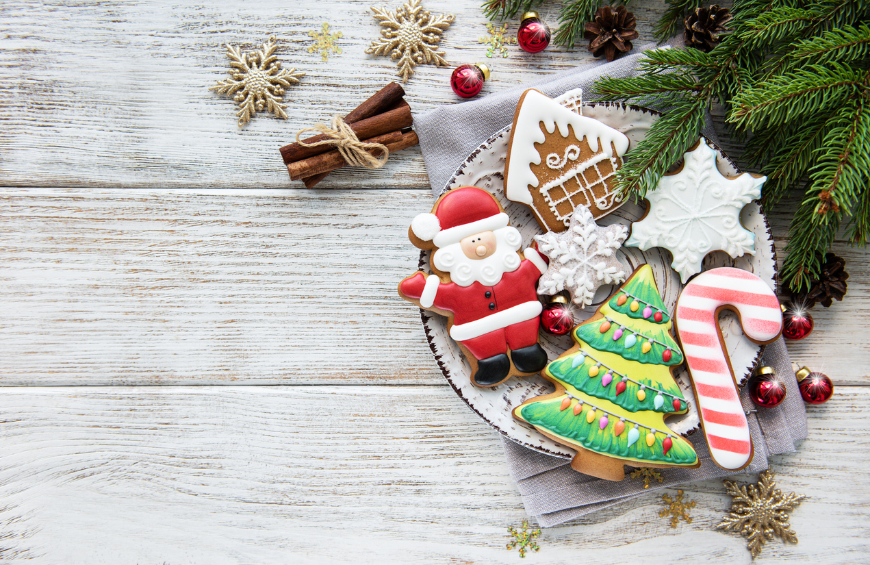 Festive decorated Christmas cookies on a plate with cinnamon sticks and pine branches nearby.
