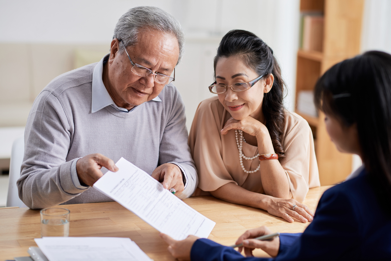 Elderly couple reviewing documents with a financial advisor at a wooden table