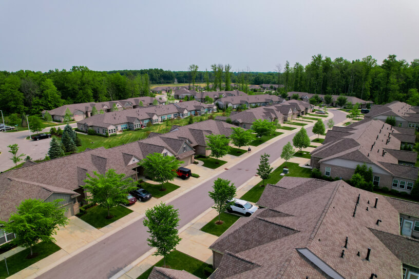 Aerial view of a neighborhood with rows of similar houses, trees, and parked cars along the street.
