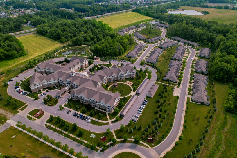 Aerial view of a large residential complex surrounded by green fields and dense forested areas.