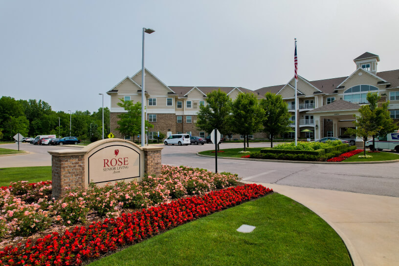 Exterior view of Rose Senior Living facility with landscaped gardens and flagpole
