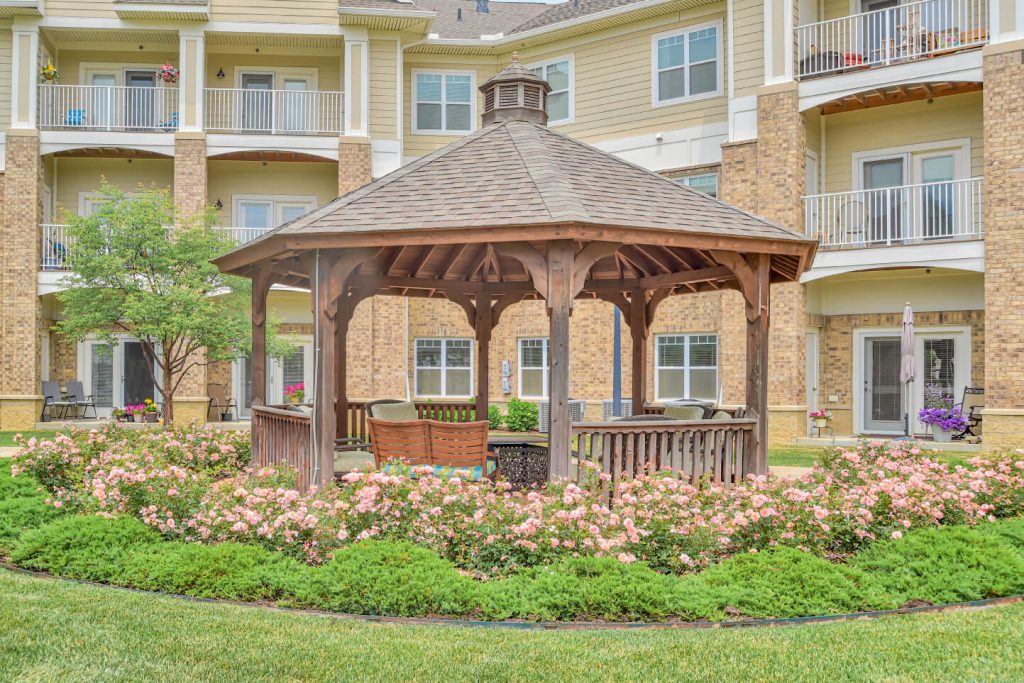 Wooden gazebo surrounded by blooming flowers in the courtyard of an apartment complex.